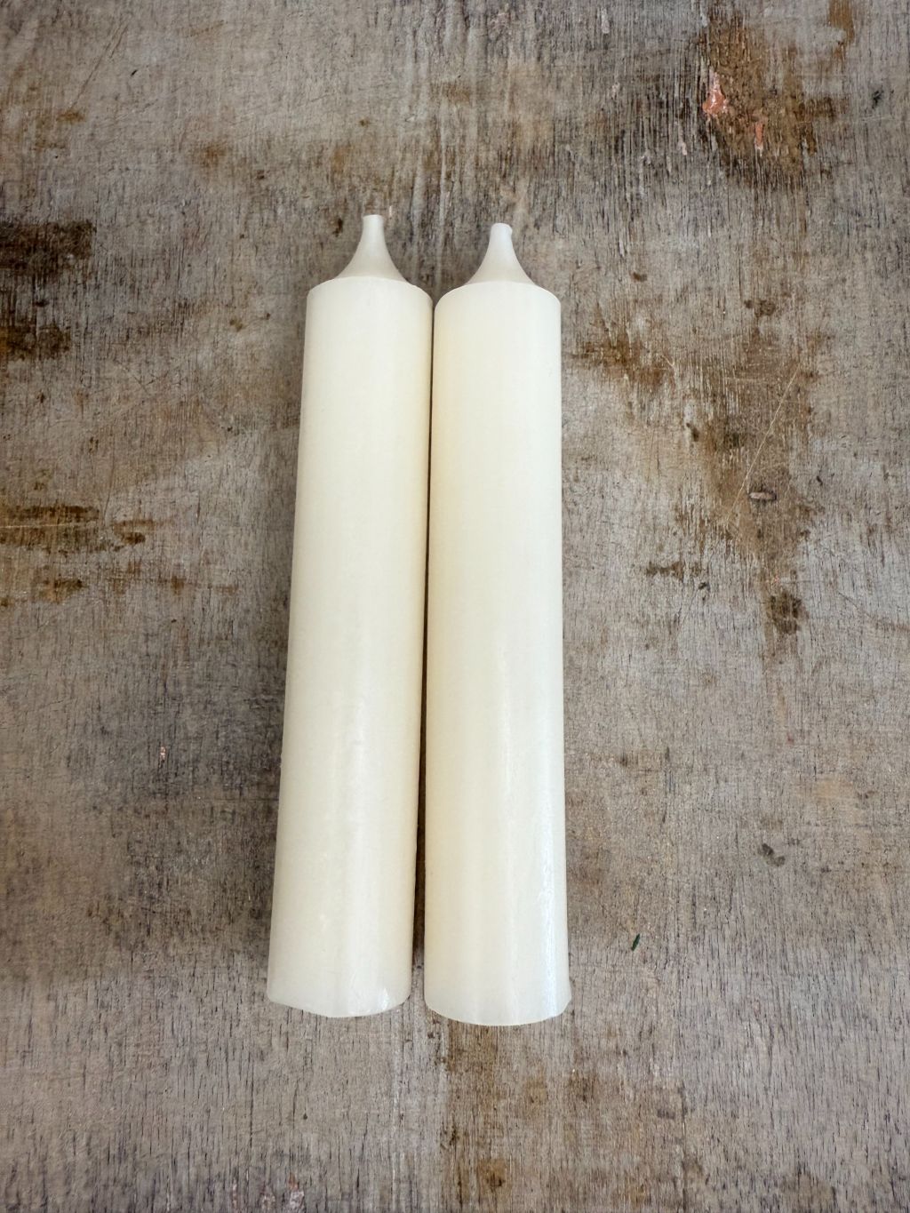 Twee champagnekleurige dinerkaarsen met afgeronde top, liggend op een verweerd houten oppervlak met warme tint.