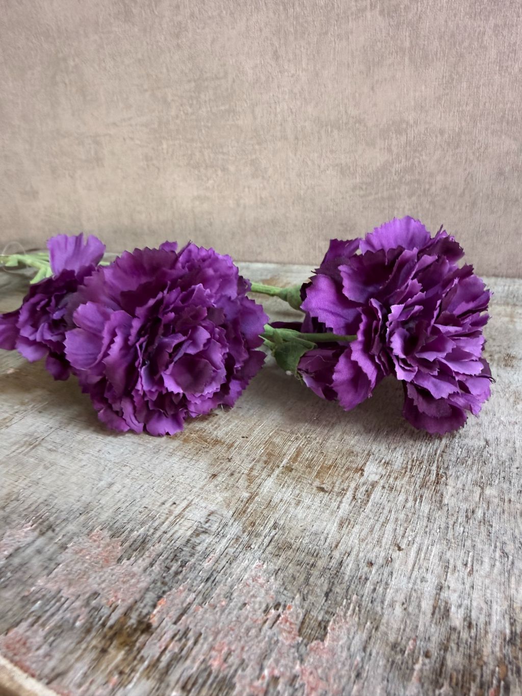 Paarse kunstbloem anjer met volle gelaagde bloemblaadjes, liggend op een houten ondergrond.