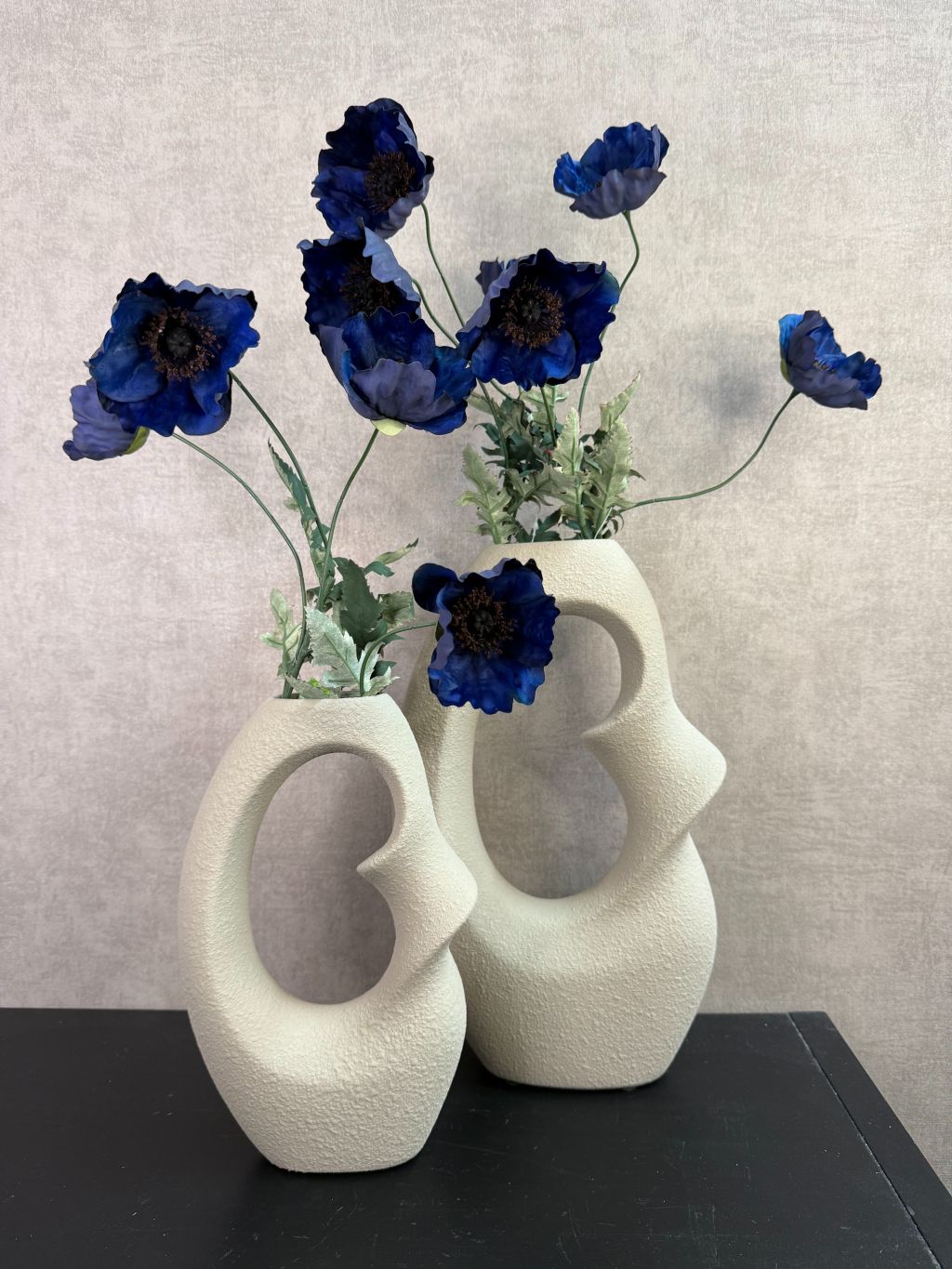 Set van twee beige keramieken vazen met kunstbloemen in verschillende formaten op een houten ondergrond