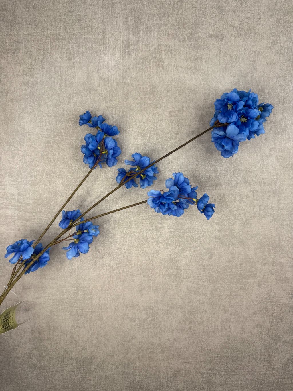 Zijden bloesemtak met helderblauwe bloemen en een fijne vertakking tegen een neutrale achtergrond.