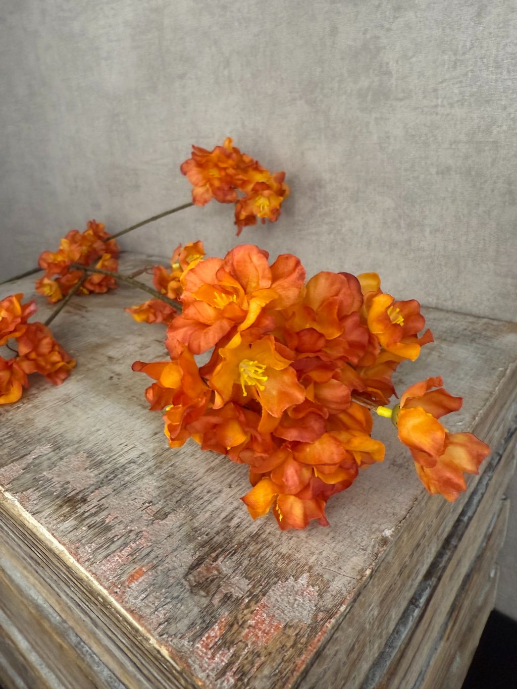 Zijden bloesemtak met oranje bloemen liggend op een houten oppervlak, met levendige bloesems en subtiel groene steel.