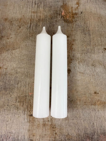 Twee witte dinerkaarsen op een houten ondergrond, klassiek en sfeervol voor elke interieurstijl.