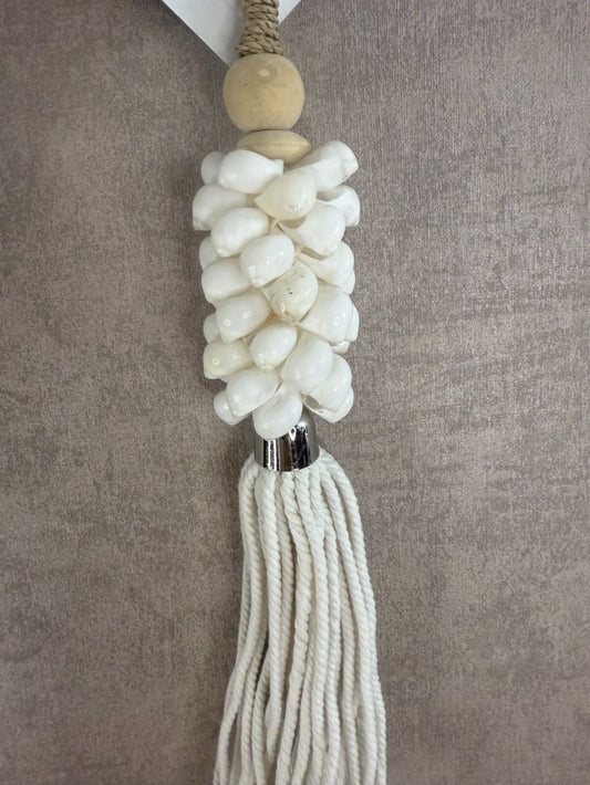 Witte hanger van schelpen en katoen met houten kraal en touw, hangend tegen een neutrale achtergrond.