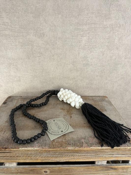 Zwart-witte decoratieve ketting met houten kralen, witte schelpen en zwarte kwast, handgemaakt.