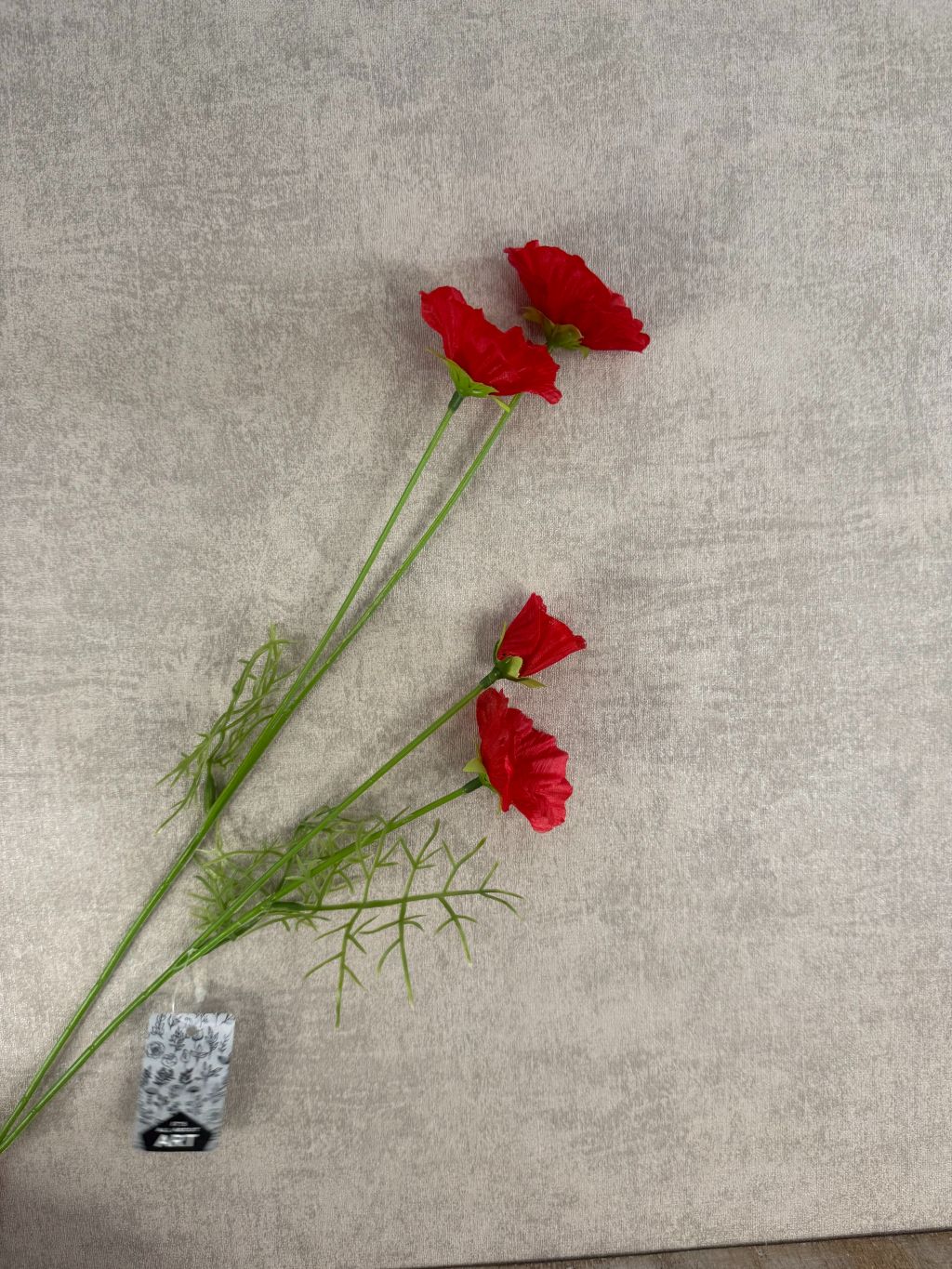 Rode kunstklaproos met drie bloemen en fijne bladeren op grijze ondergrond.