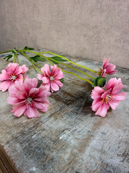 Roze kunstbloem korenbloem met groene stelen en meerdere bloemen op een grijze achtergrond.