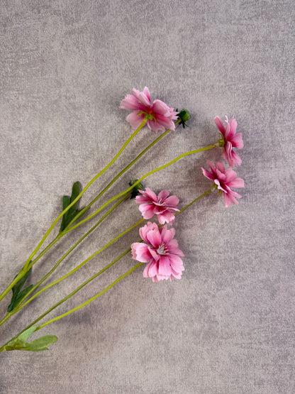 Roze kunstbloem korenbloem met groene stelen en meerdere bloemen op een grijze achtergrond.