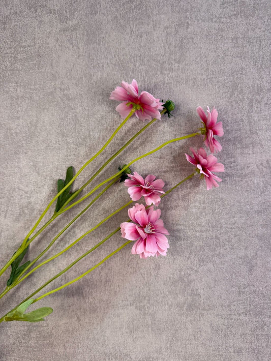 Roze kunstbloem korenbloem met groene stelen en meerdere bloemen op een grijze achtergrond.
