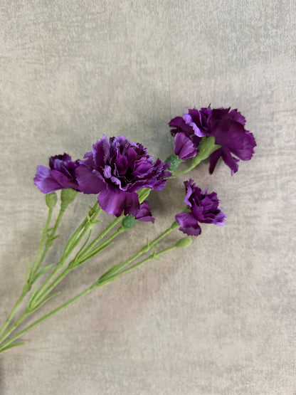 Paarse kunstbloem anjer met volle gelaagde bloemblaadjes, liggend op een houten ondergrond.
