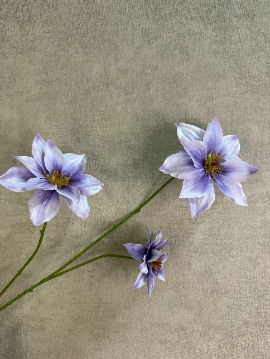 Lila kunstbloem clematis met grote open bloem en subtiel kleurverloop, liggend op een houten ondergrond.