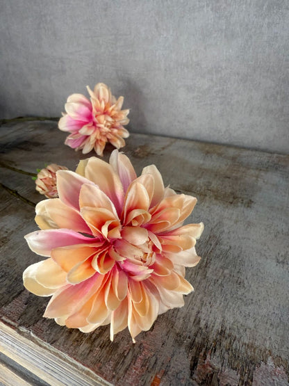 Kunstbloem dahlia met champagne- en rozekleurige bloemblaadjes op lange steel tegen een zachte grijze achtergrond.