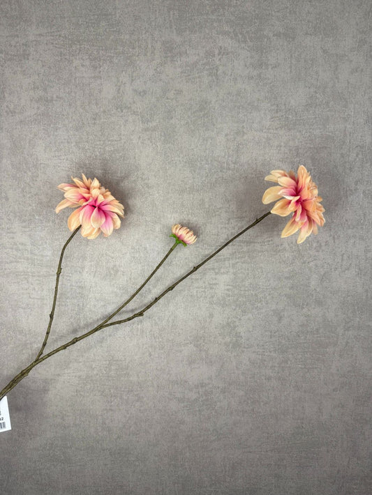 Kunstbloem dahlia met champagne- en rozekleurige bloemblaadjes op lange steel tegen een zachte grijze achtergrond.