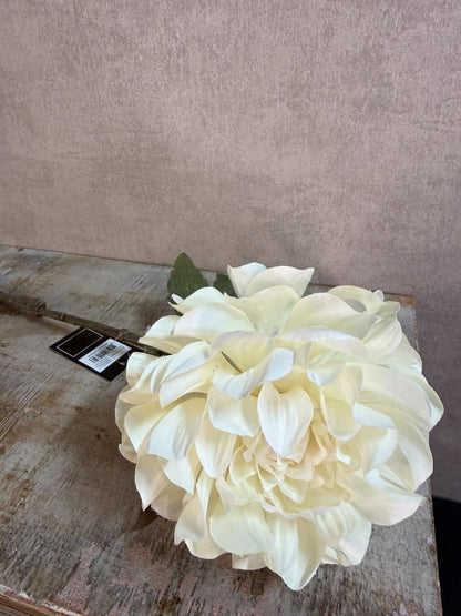 Crèmekleurige kunstbloem dahlia met volle bloem en groene bladeren tegen een neutrale achtergrond.
