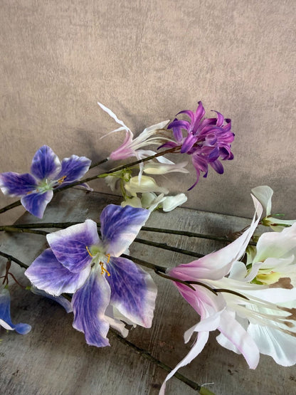 Extra lange kunstbloem met gemengde bloemen in wit, blauw en paars, liggend op een neutrale achtergrond.
