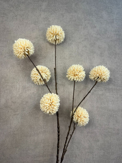 Crèmekleurige kunsttak met meerdere pompomvormige bloemen op donkere steel, tegen een neutrale achtergrond.