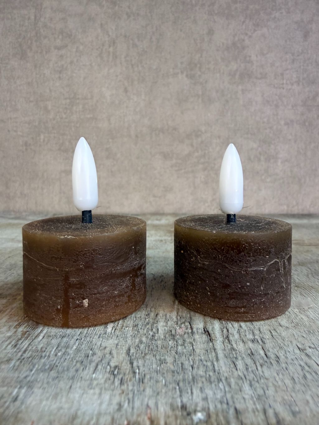 Twee bruine led waxinelichtjes met witte vlam op een houten ondergrond.