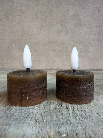 Twee bruine led waxinelichtjes met witte vlam op een houten ondergrond.