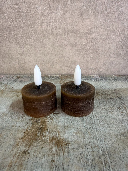Twee bruine led waxinelichtjes met witte vlam op een houten ondergrond.
