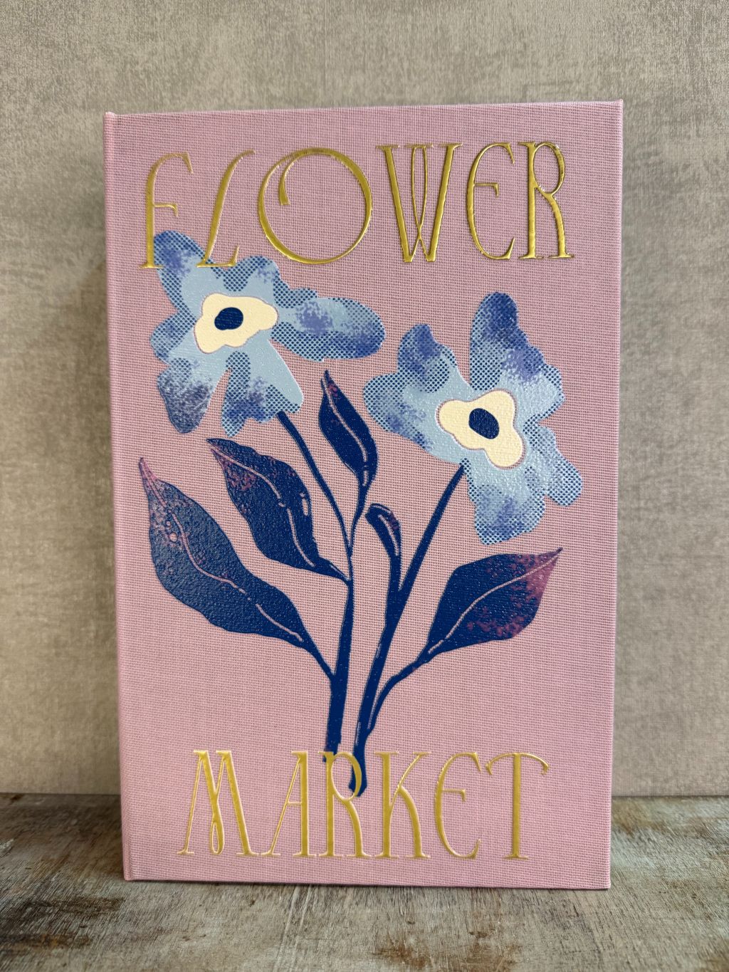 Roze opbergboek Flower Market met bloemenillustratie en gouden tekst, staand op een houten ondergrond.