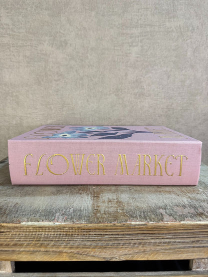 Roze opbergboek Flower Market met bloemenillustratie en gouden tekst, staand op een houten ondergrond.