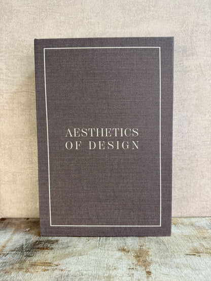 Bruin opbergboek Aesthetics of Design met witte omlijning en tekst, staand op een houten ondergrond.