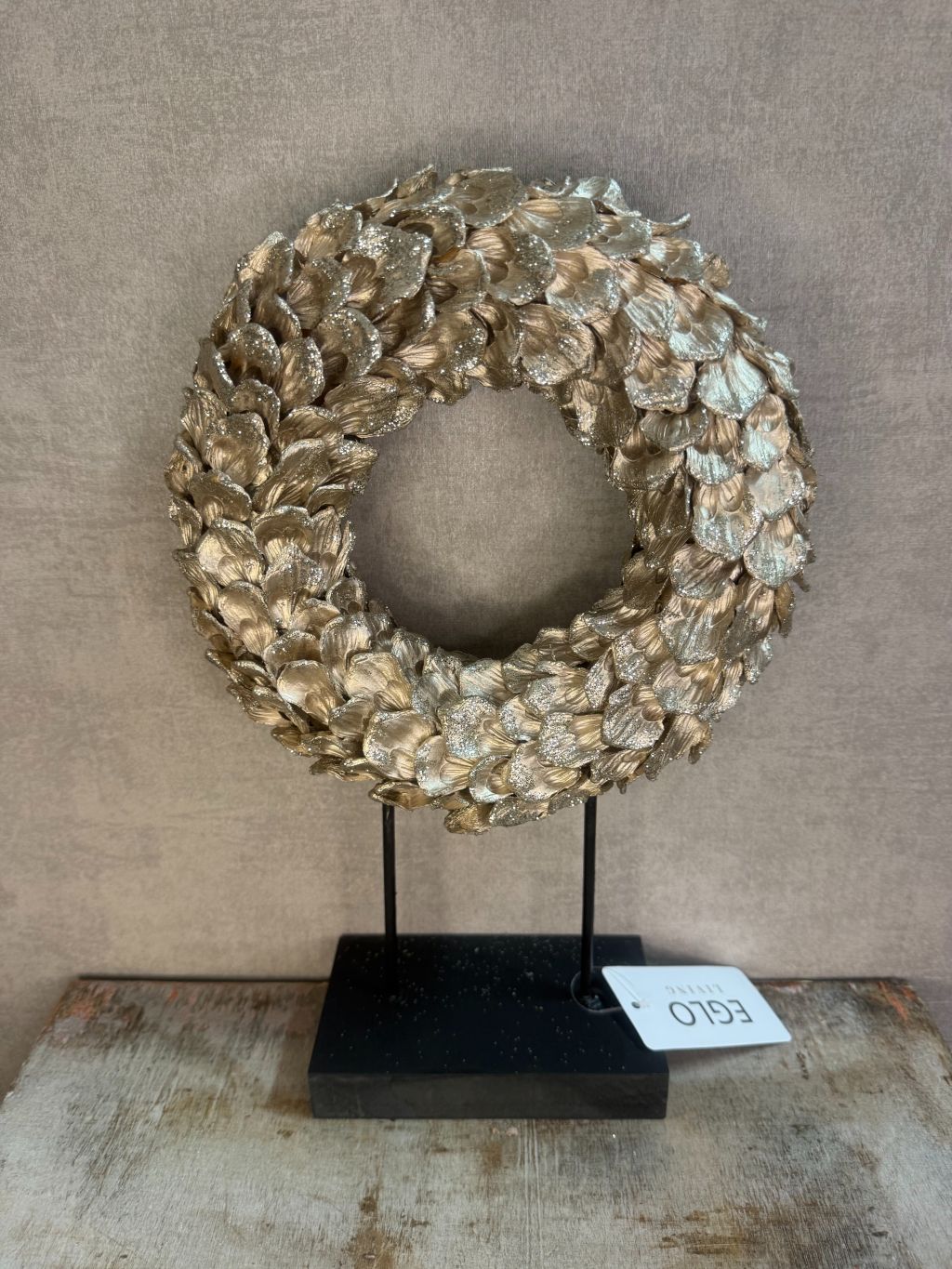 Ornament Krans glitter champagne – ronde decoratie met glanzende bladeren op zwarte standaard van Eglo Living.