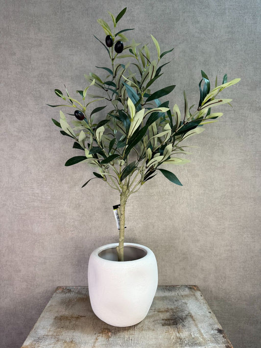 Kunst olijfplant met groene bladeren en zwarte olijven in een witte pot op een houten ondergrond.