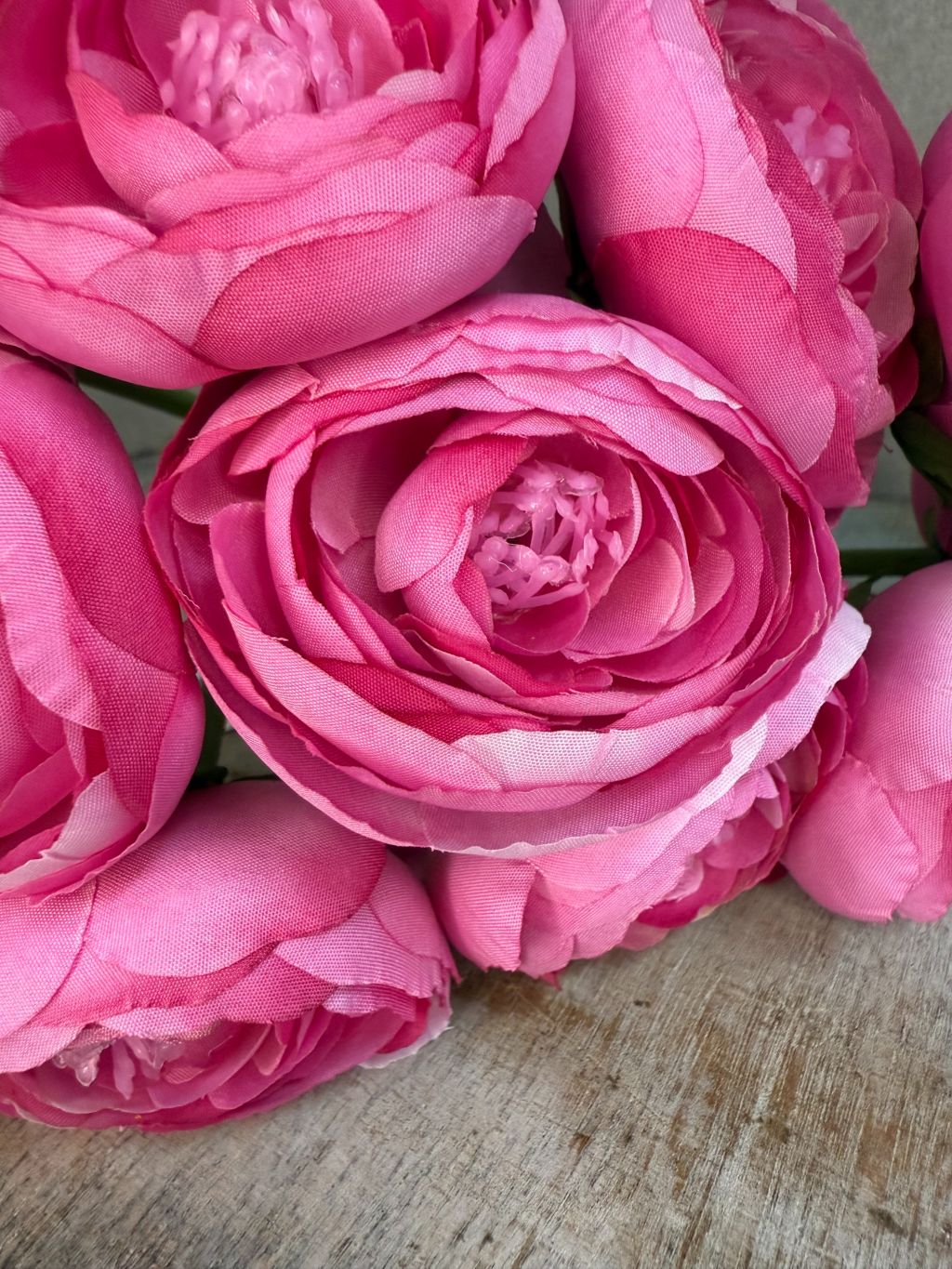 Meerdere kunstbloemen ranonkel in roze tint met realistische bloemstructuur en groene steel, liggend op een houten oppervlak.