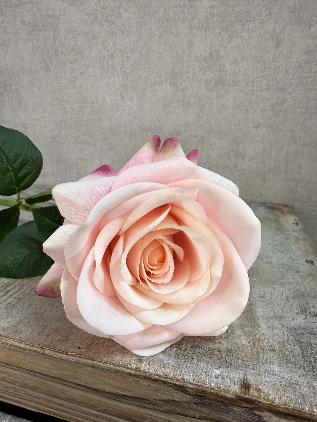 Roze real touch kunstroos van Mica met groene steel en bladeren op een grijze achtergrond.