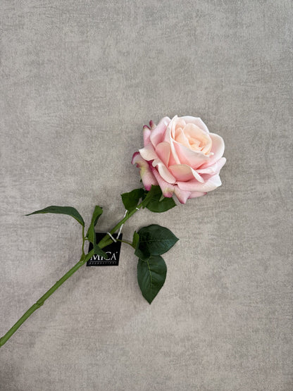 Roze real touch kunstroos van Mica met groene steel en bladeren op een grijze achtergrond.
