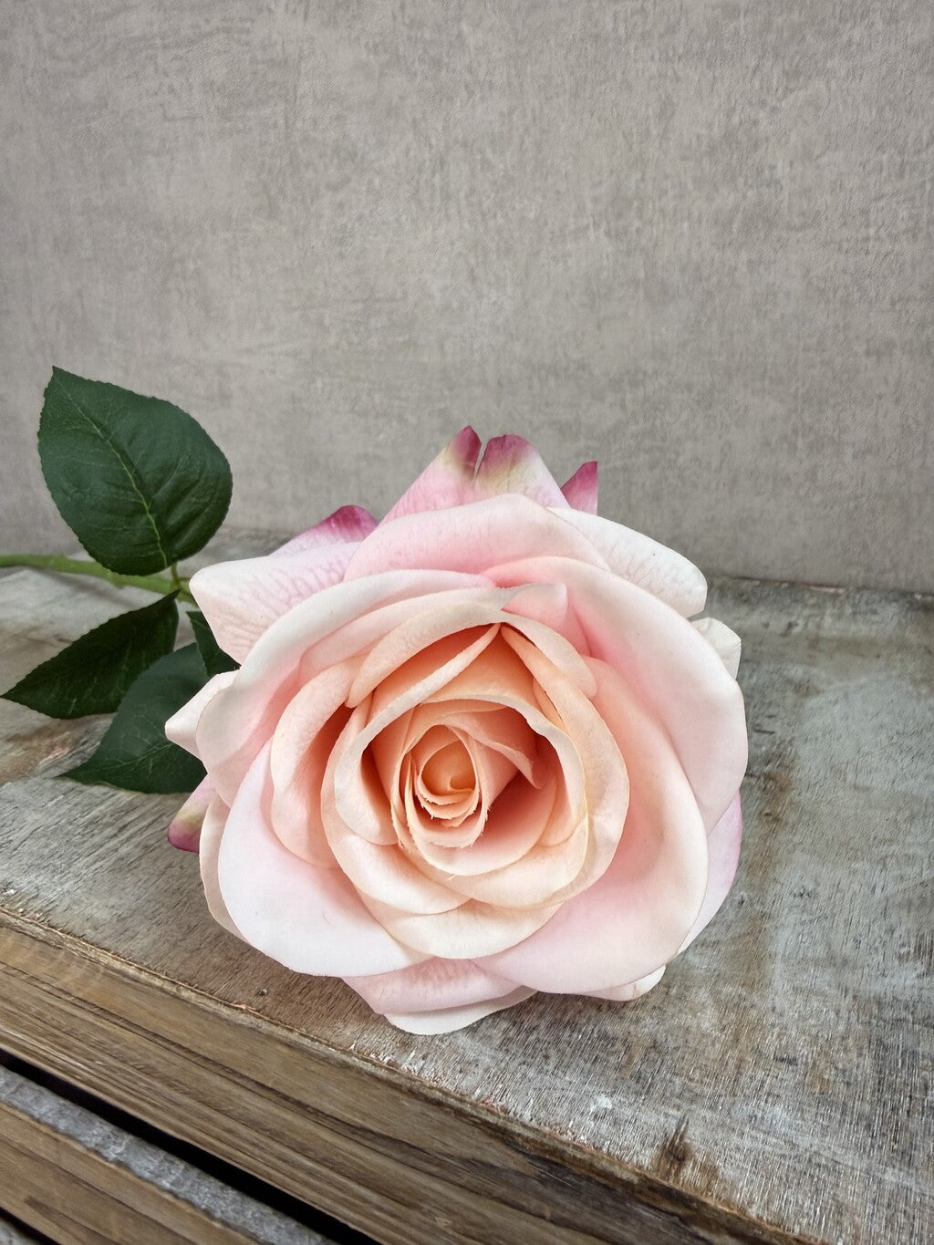 Roze real touch kunstroos van Mica met groene steel en bladeren op een grijze achtergrond.