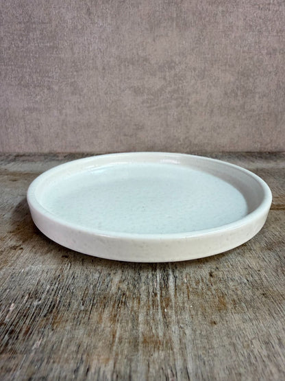 Wit keramieken schaaltje met opstaande rand op een houten ondergrond tegen een neutrale achtergrond.