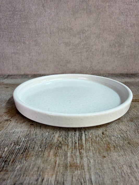 Wit keramieken schaaltje met opstaande rand op een houten ondergrond tegen een neutrale achtergrond.