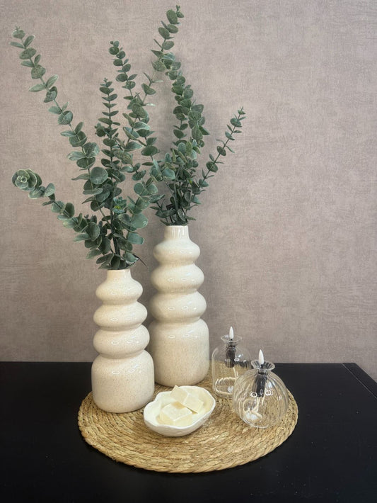 Tafel decoratie set Lovi – beige vazen met eucalyptus­takken, LED-oliekaarsjes en amberblokjes op gevlochten placemat.