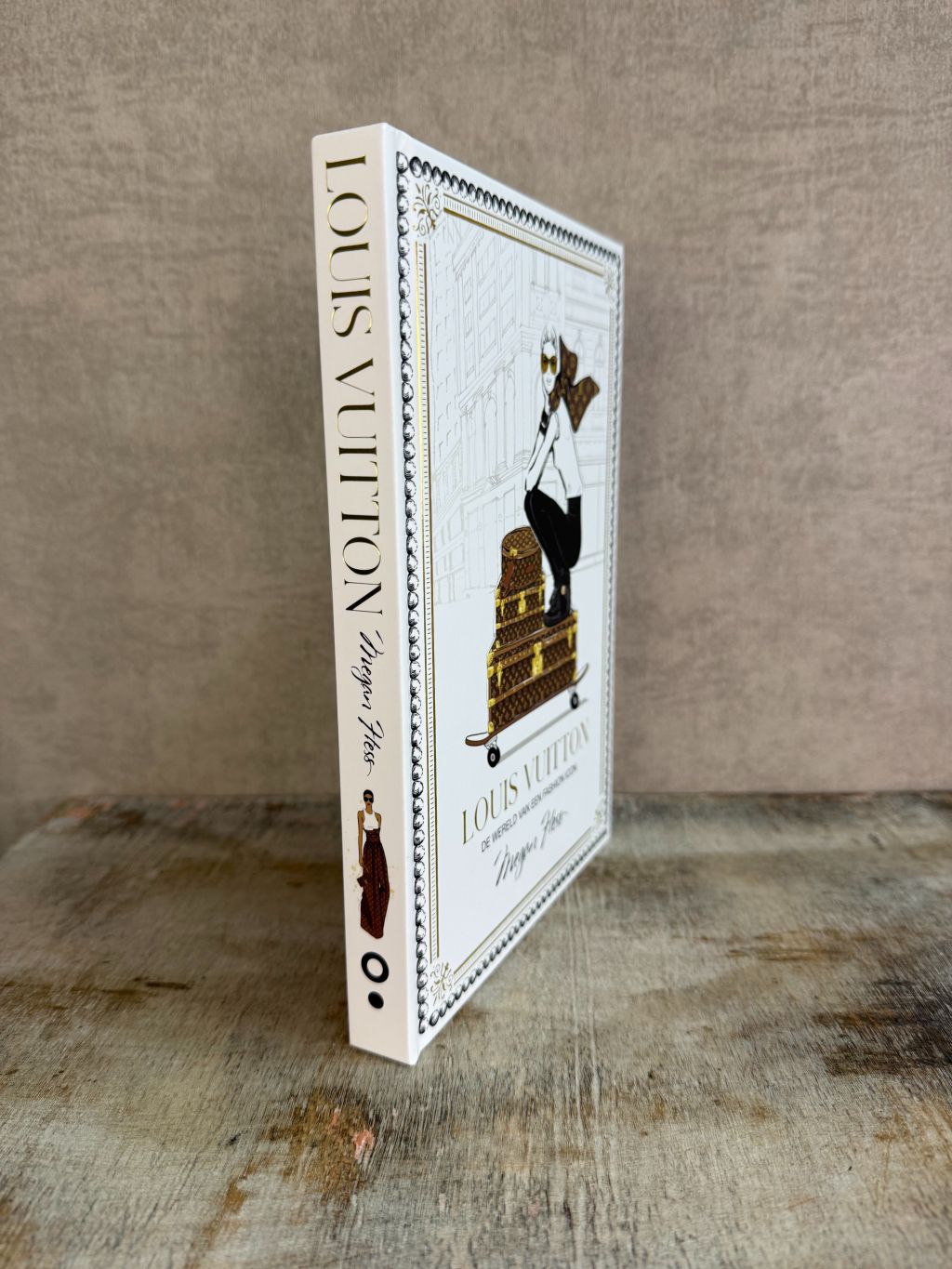 Wit tafelboek over Louis Vuitton met illustratie van een vrouw op koffers en gouden details op de omslag.