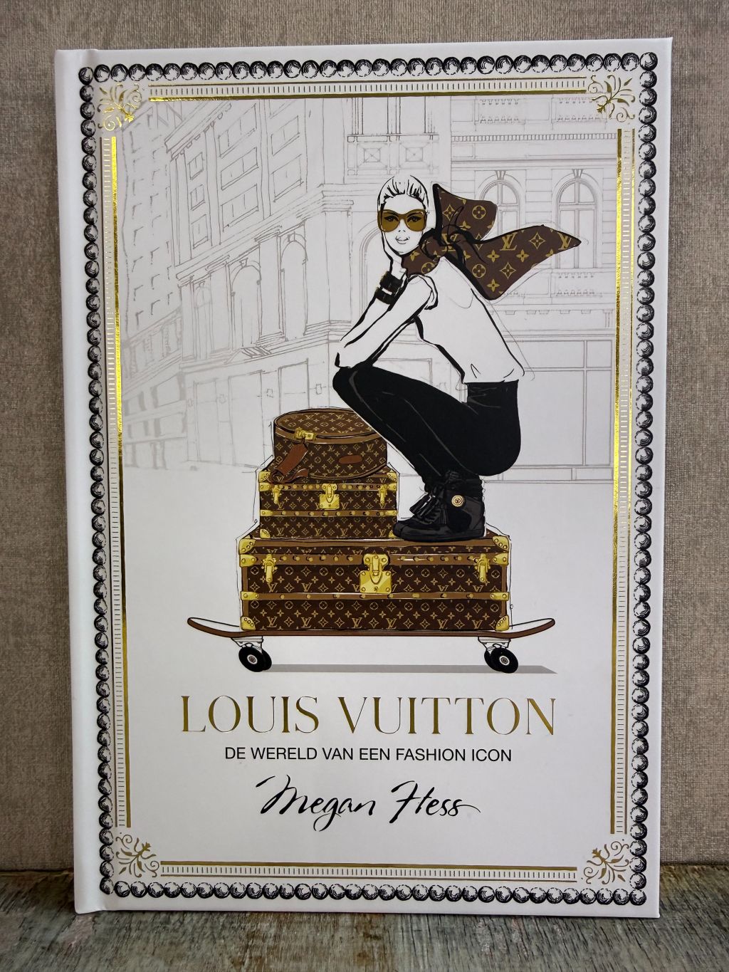 Wit tafelboek over Louis Vuitton met illustratie van een vrouw op koffers en gouden details op de omslag.