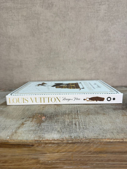 Wit tafelboek over Louis Vuitton met illustratie van een vrouw op koffers en gouden details op de omslag.