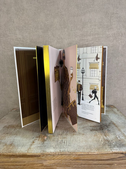 Wit tafelboek over Louis Vuitton met illustratie van een vrouw op koffers en gouden details op de omslag.