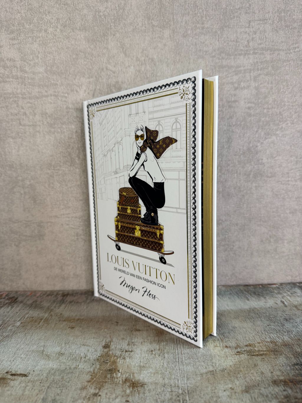 Wit tafelboek over Louis Vuitton met illustratie van een vrouw op koffers en gouden details op de omslag.