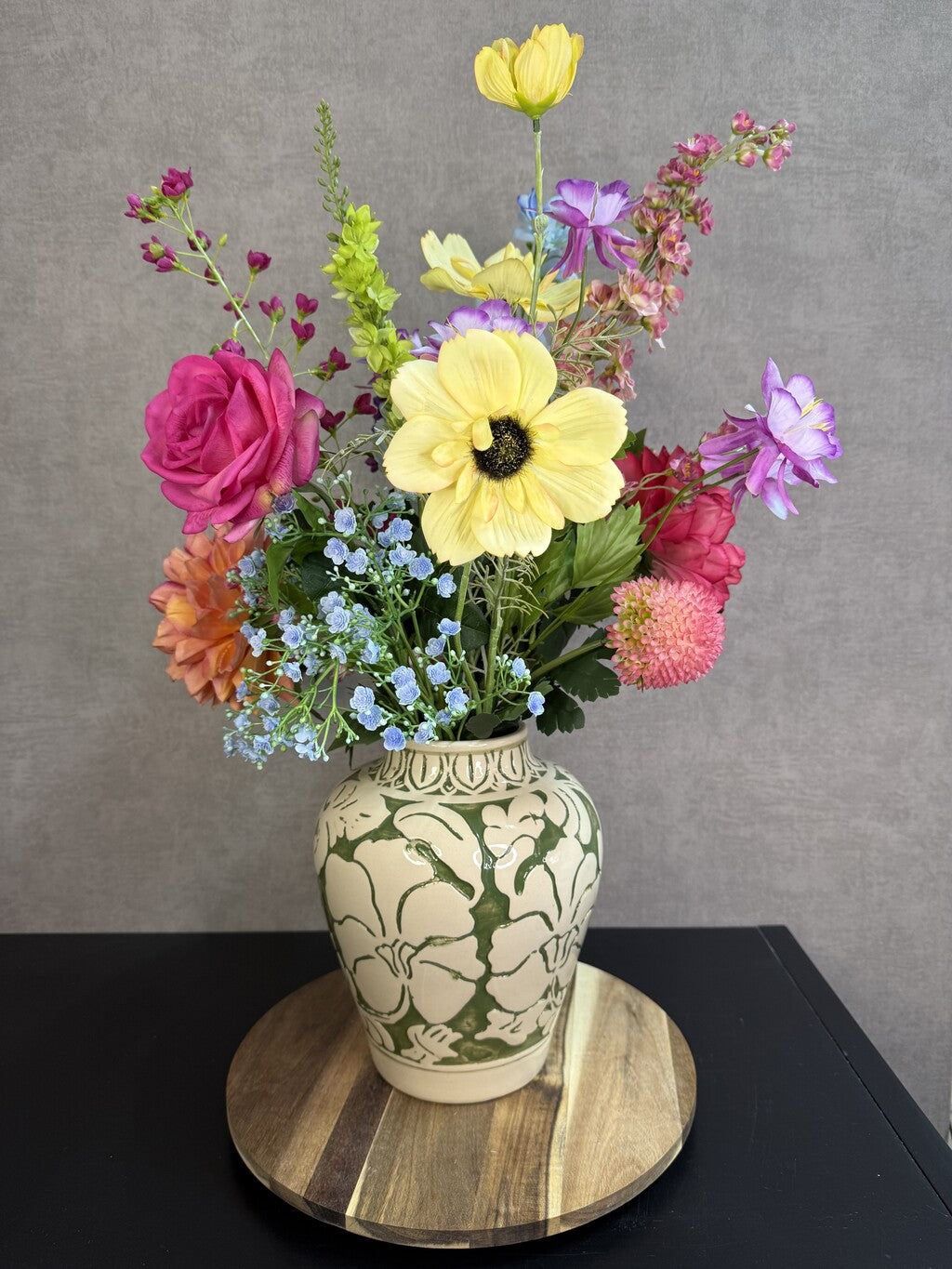 Beige keramieken vaas met groen bloemmotief van Mica met kunstbloemen op een houten ondergrond.