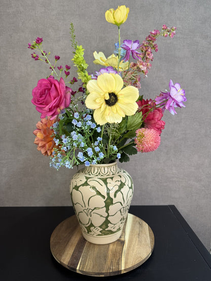 Beige keramieken vaas met groen bloemmotief van Mica met kunstbloemen op een houten ondergrond.