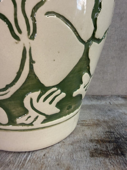 Beige keramieken vaas met groen bloemmotief van Mica op een houten ondergrond.