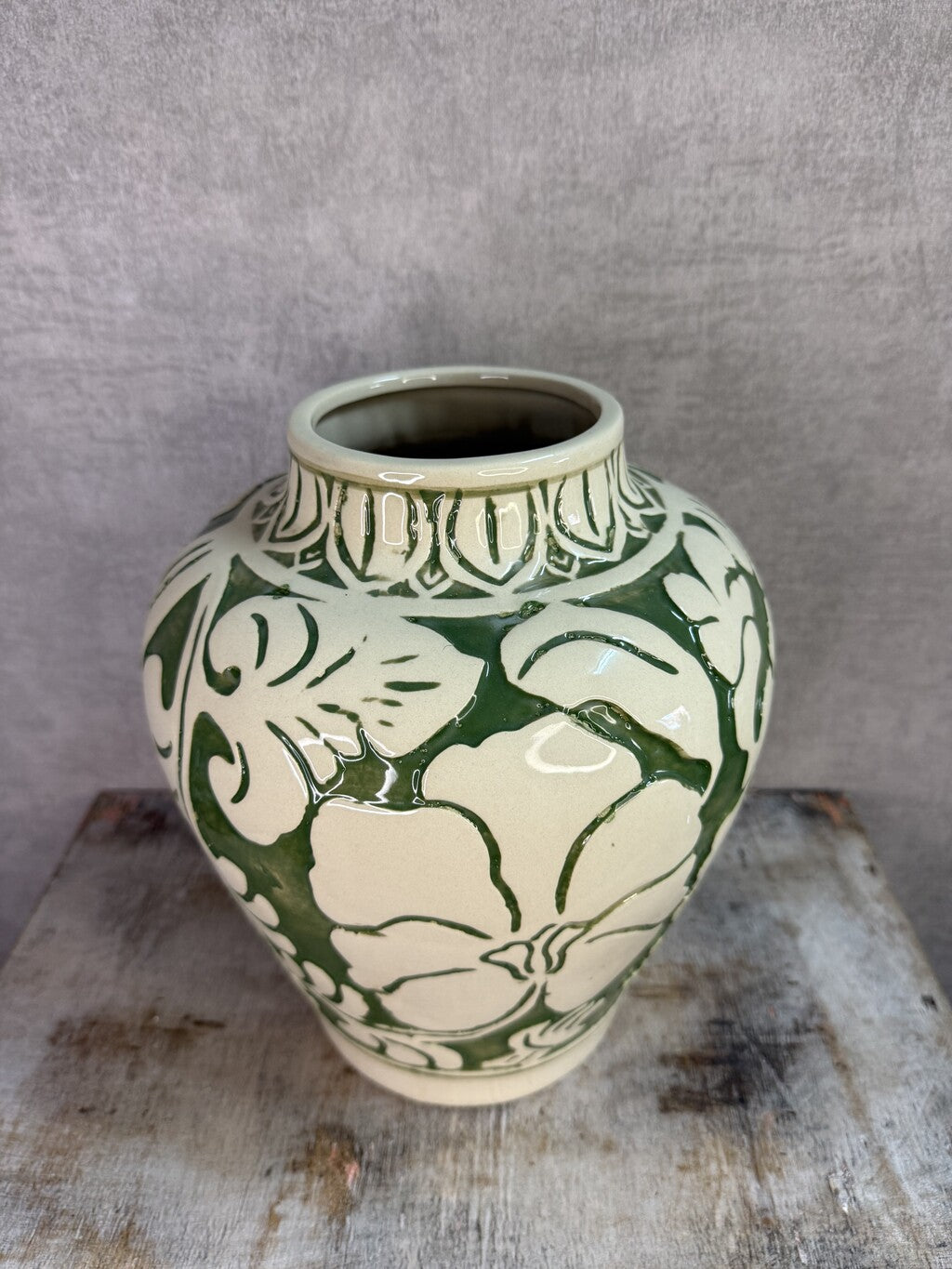 Beige keramieken vaas met groen bloemmotief van Mica op een houten ondergrond.