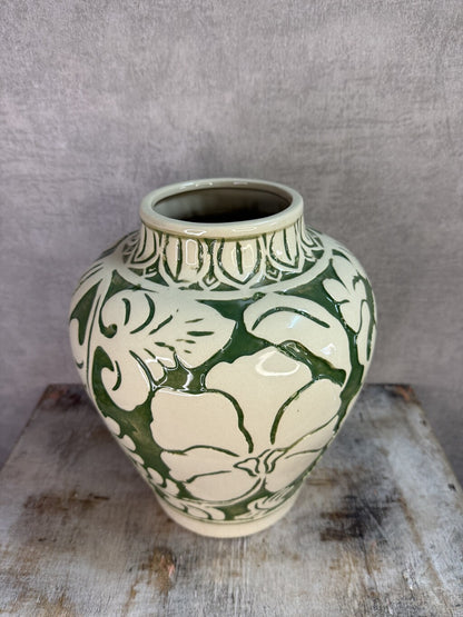 Beige keramieken vaas met groen bloemmotief van Mica op een houten ondergrond.