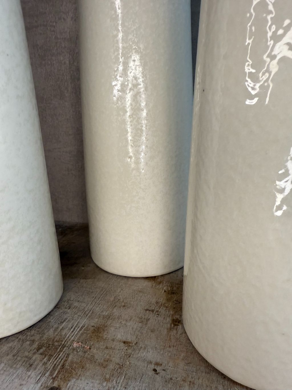 Drie crèmekleurige vazen van keramiek in verschillende hoogtes en smalle cilindervorm, staand op een houten oppervlak.