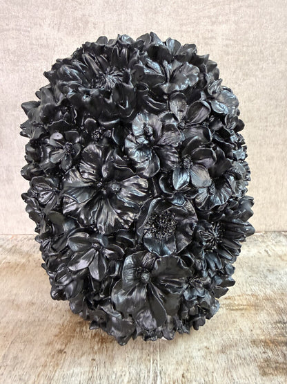 Zwarte polyresin vaas met bloemreliëf op een houten ondergrond.