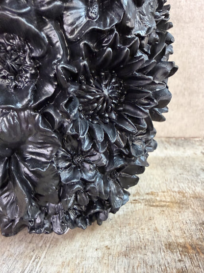 Zwarte polyresin vaas met bloemreliëf op een houten ondergrond.
