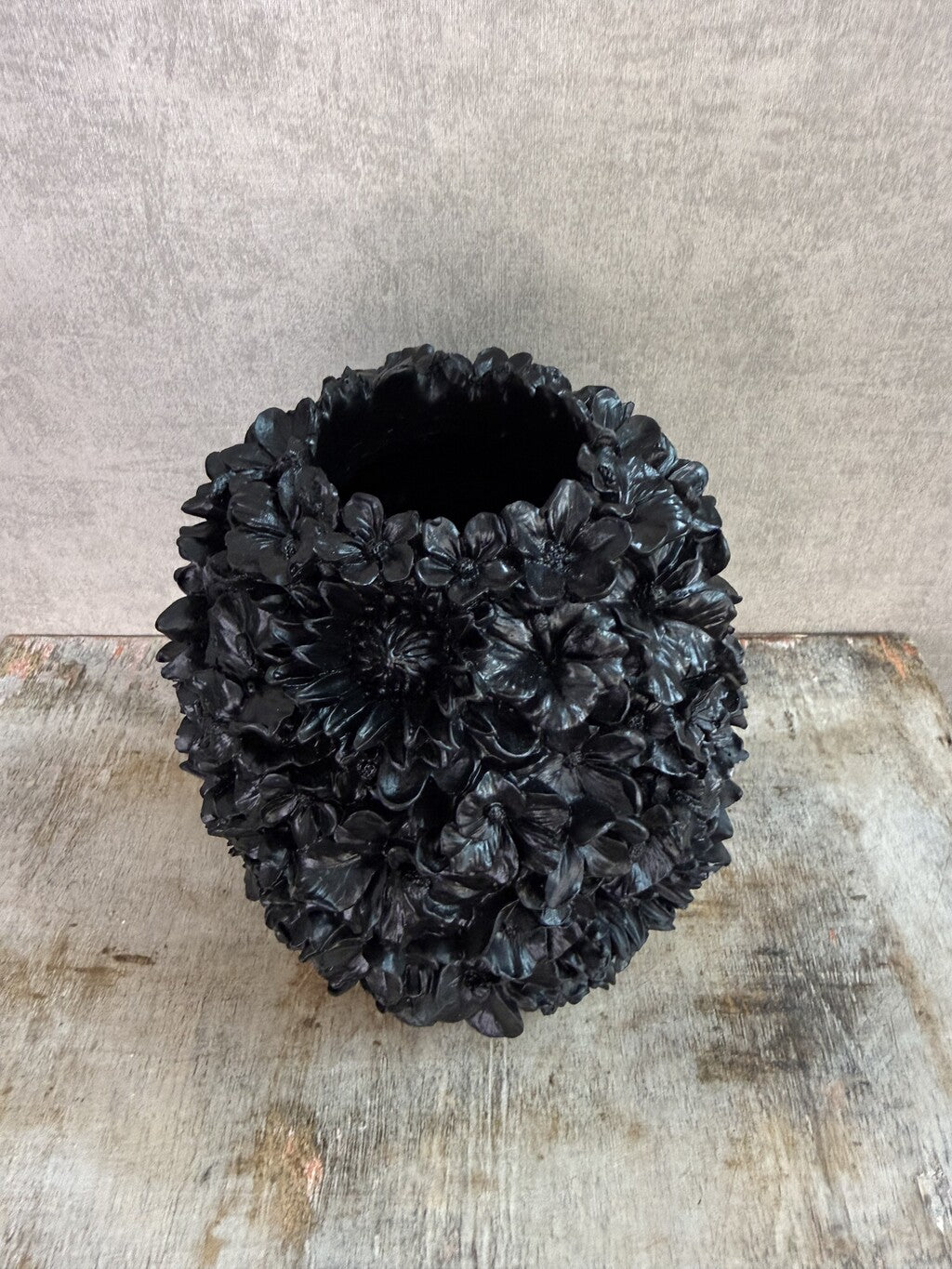 Zwarte polyresin vaas met bloemreliëf op een houten ondergrond.