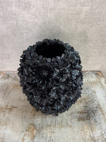 Zwarte polyresin vaas met bloemreliëf op een houten ondergrond.