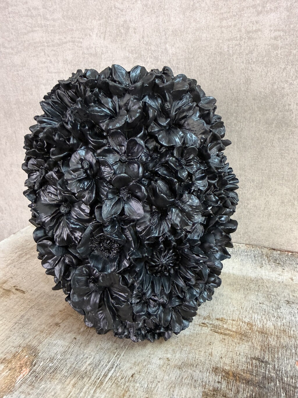Zwarte polyresin vaas met bloemreliëf op een houten ondergrond.